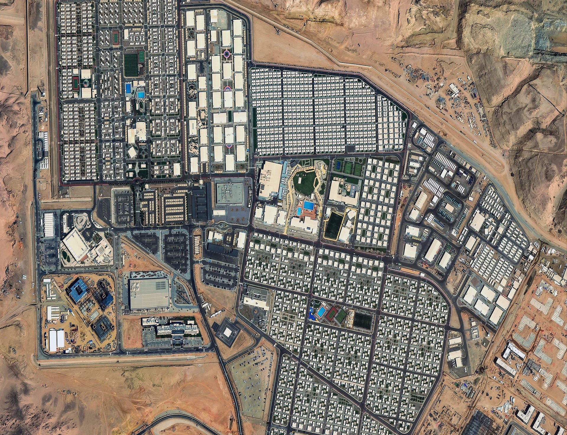 Satellite image of a densely developed urban or industrial area with numerous buildings and infrastructure, overlaid with three text boxes outlining flexible satellite tasking options: Single Shot, Select Plus, and Select (described as optimized for mapping and weather-independent tasking, ensuring clear imagery).