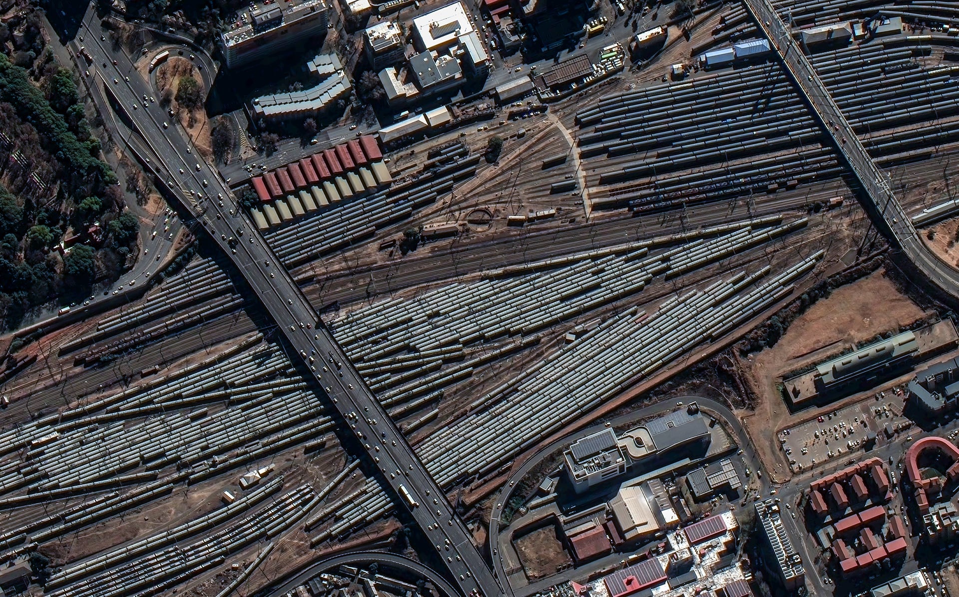 Satellite image showing a large railway yard with numerous trains parked on multiple tracks, overlaid with three text boxes outlining flexible satellite tasking options: Single Shot, Select Plus (described as balanced for timeliness and cloud-free, with priority over Select in queue), and Select.