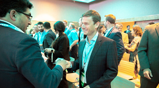 Out-of-focus shot of several people in business attire interacting in a brightly lit, modern office or event space.
